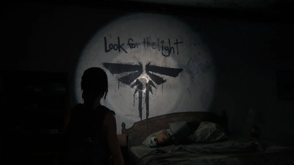 Screenshot from 'The Last of Us' videgame 2013. Ellie illuminates graffiti of a firefly symbol with her torchlight. The text above reads 'Look for the light.'